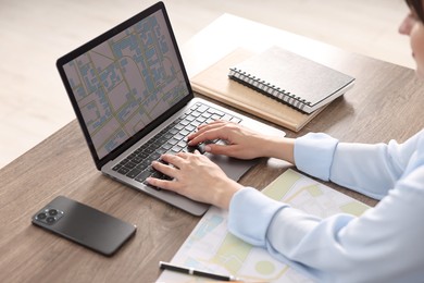 Cartographer working with cadastral map on laptop at wooden table in office, closeup
