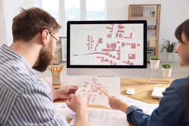 Cartographers working with cadastral maps at table in office, back view