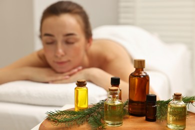 Aromatherapy. Woman relaxing on massage couch in spa salon, focus on bottles of essential oils and fir branches