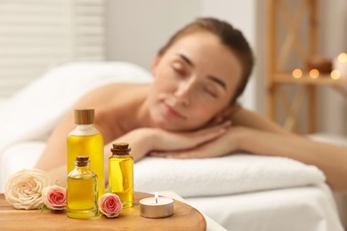 Aromatherapy. Woman relaxing on massage couch in spa salon, focus on bottles of essential oils, burning candle and rose flowers