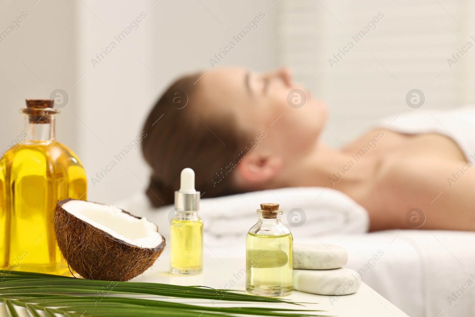 Photo of Aromatherapy. Woman relaxing on massage couch in spa salon, focus on bottles of essential oils, coconut and stones