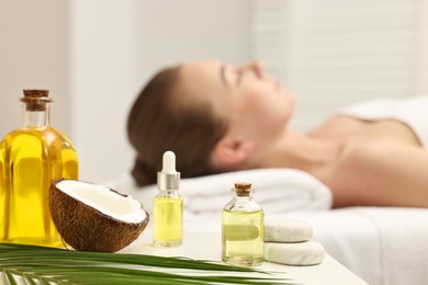 Photo of Aromatherapy. Woman relaxing on massage couch in spa salon, focus on bottles of essential oils, coconut and stones