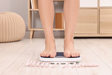 Photo of Woman standing on floor scale and measuring tape at home, closeup. Weight control