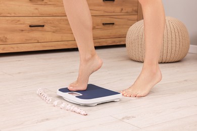 Woman stepping on floor scale and measuring tape at home, closeup. Weight control