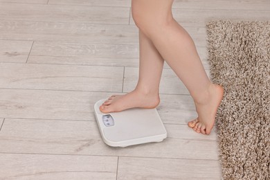 Woman stepping on floor scale at home, closeup. Space for text