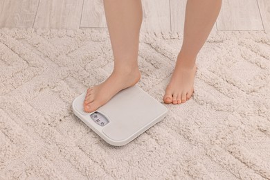 Woman stepping on floor scale at home, closeup