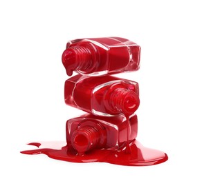 Red nail polishes dripping from bottles on white background