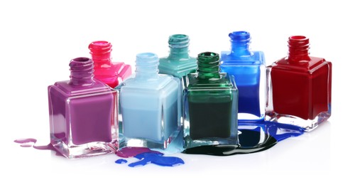 Puddle of different bright nail polishes and bottles isolated on white