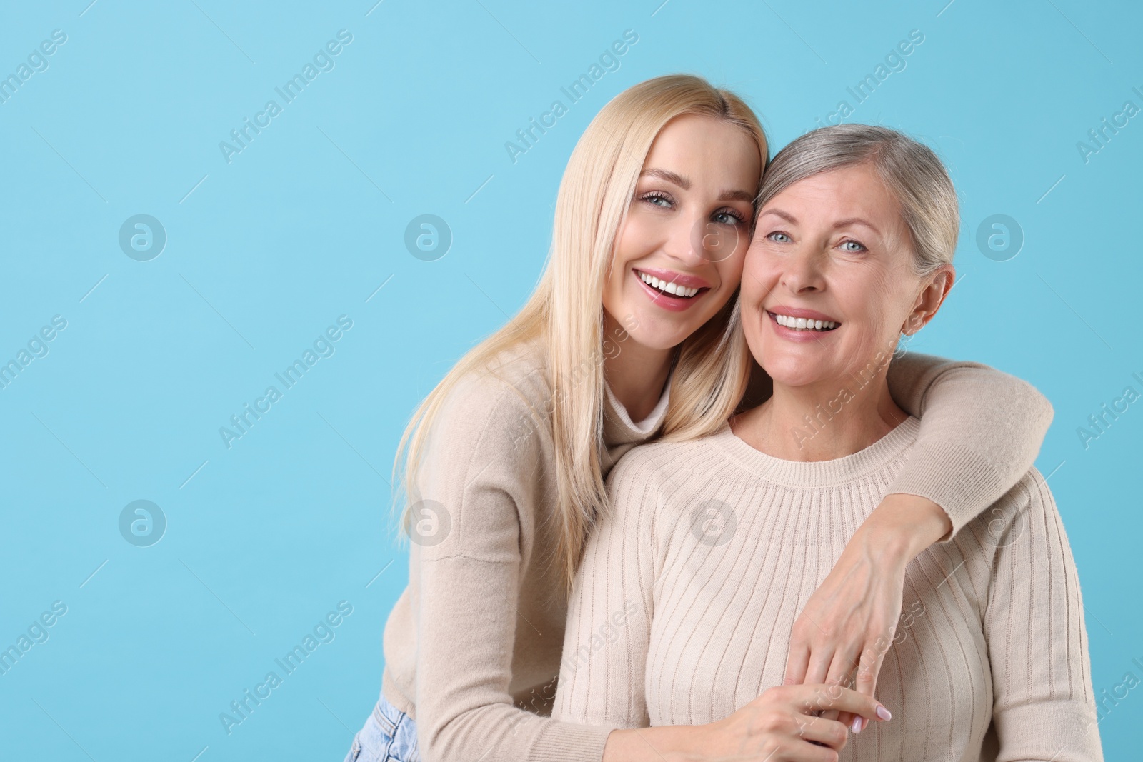 Photo of Family portrait of young woman and her mother on light blue background. Space for text