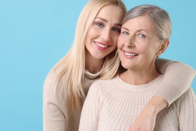 Family portrait of young woman and her mother on light blue background