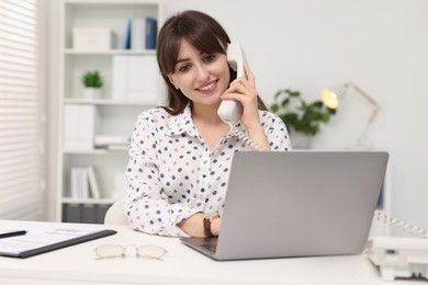 Photo of Smiling secretary talking on telephone at table in office