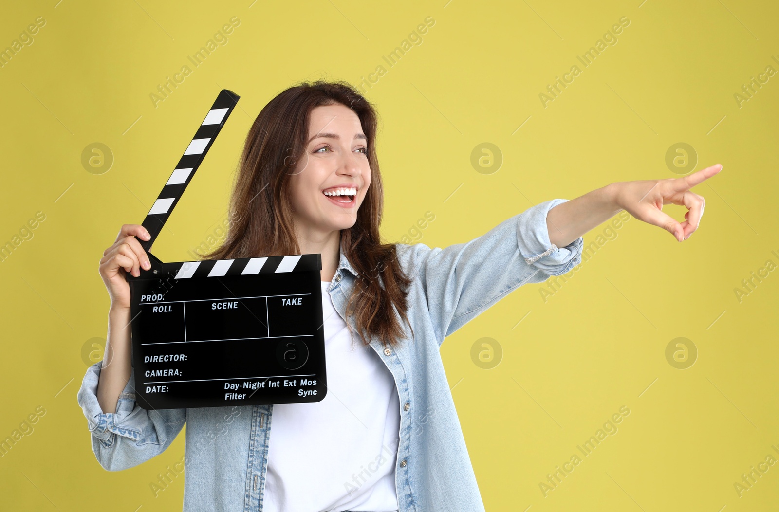 Photo of Making movie. Smiling woman with clapperboard pointing at something on yellow background