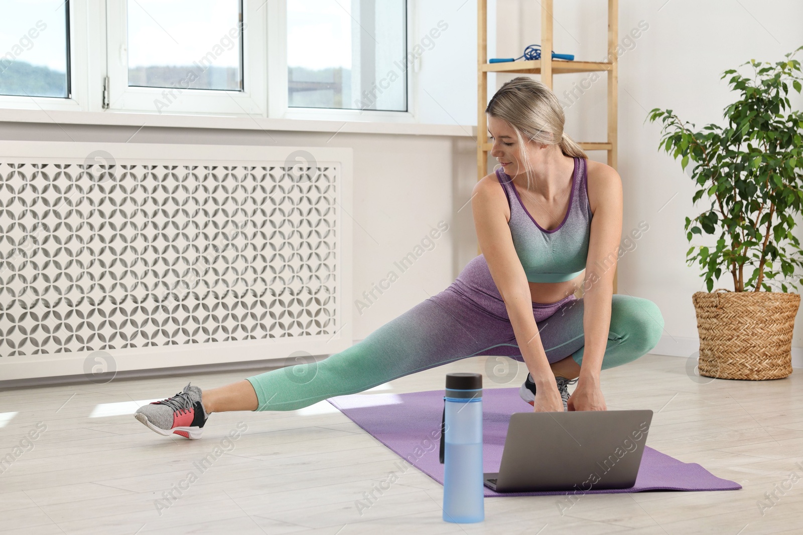 Photo of Online fitness trainer. Woman doing exercise near laptop at home