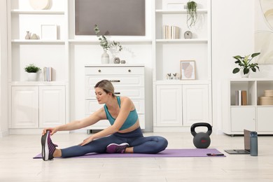 Photo of Online fitness trainer. Woman doing exercise near laptop at home