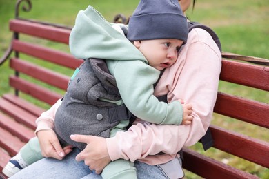 Photo of Mother holding her child in sling (baby carrier) on bench outdoors, closeup