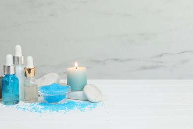 Different aromatherapy products and burning candle on white wooden table, space for text