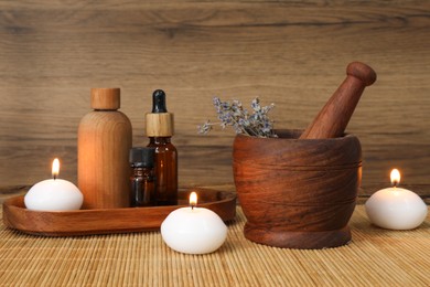 Different aromatherapy products, burning candles and mortar on table