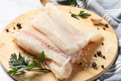 Photo of Pieces of raw cod fish, spices and parsley on table, closeup