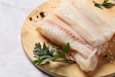 Photo of Pieces of raw cod fish, spices and parsley on white marble table, closeup