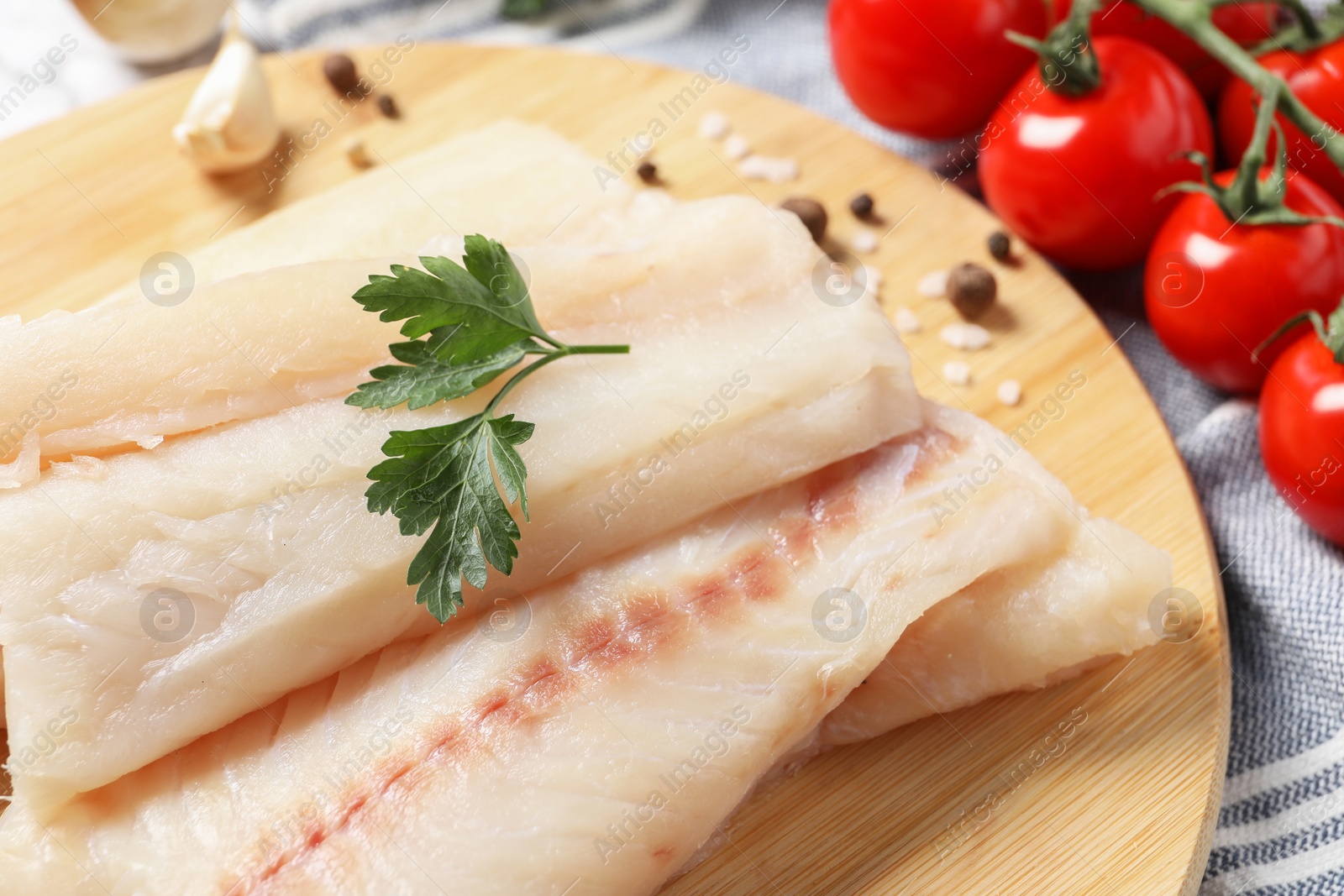 Photo of Pieces of raw cod fish, spices, parsley and tomatoes on table, closeup
