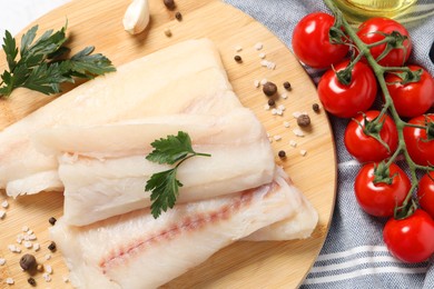 Photo of Pieces of raw cod fish, spices, parsley and tomatoes on table, top view