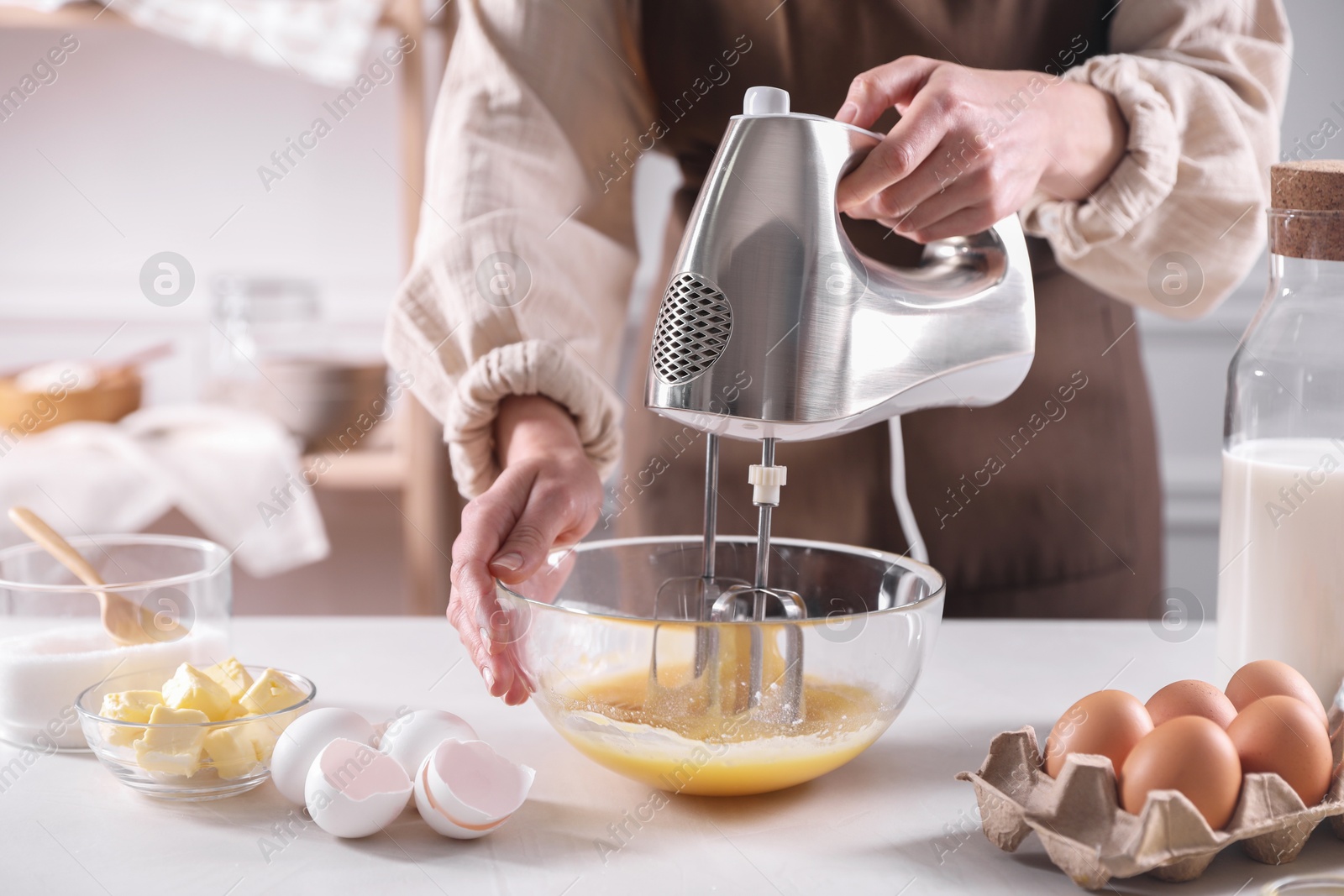 Photo of Woman making dough with mixer in bowl at table, closeup