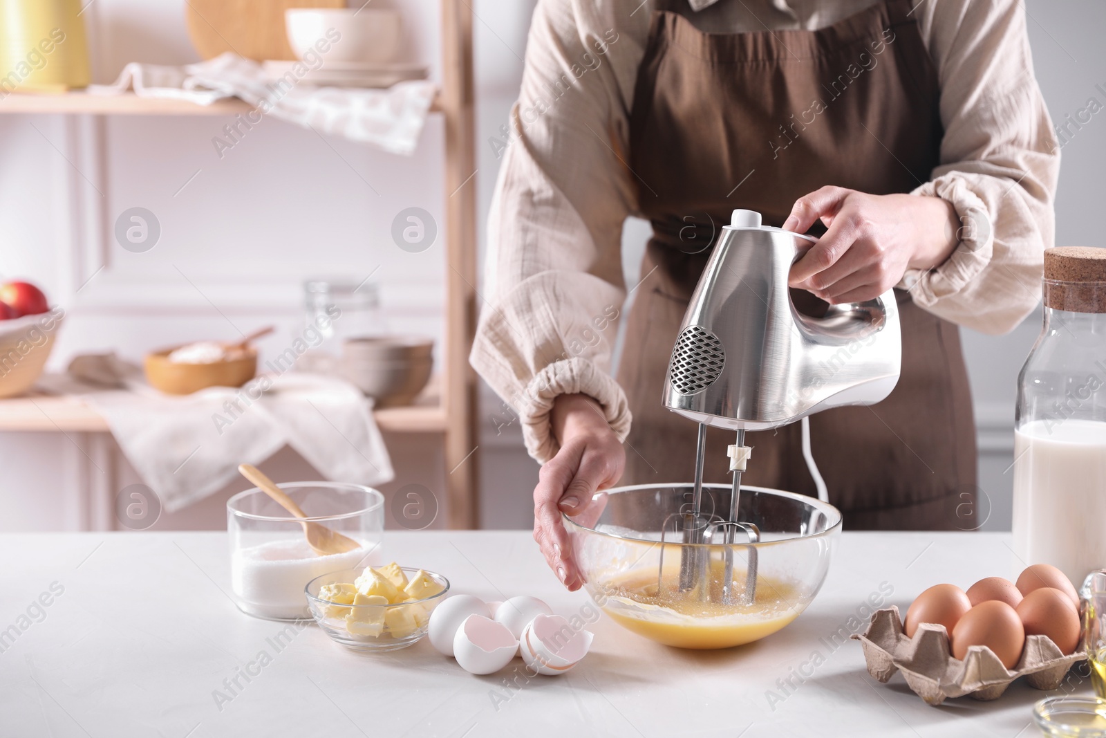 Photo of Woman making dough with mixer in bowl at table, closeup