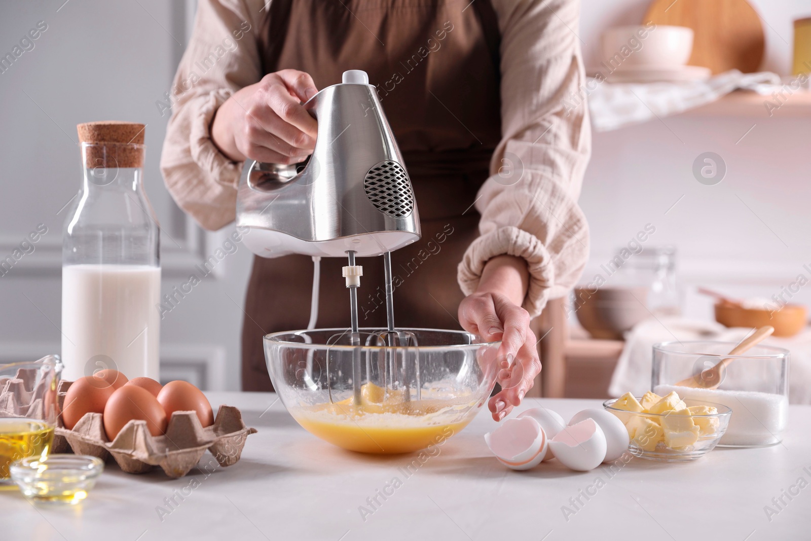 Photo of Woman making dough with mixer in bowl at table, closeup