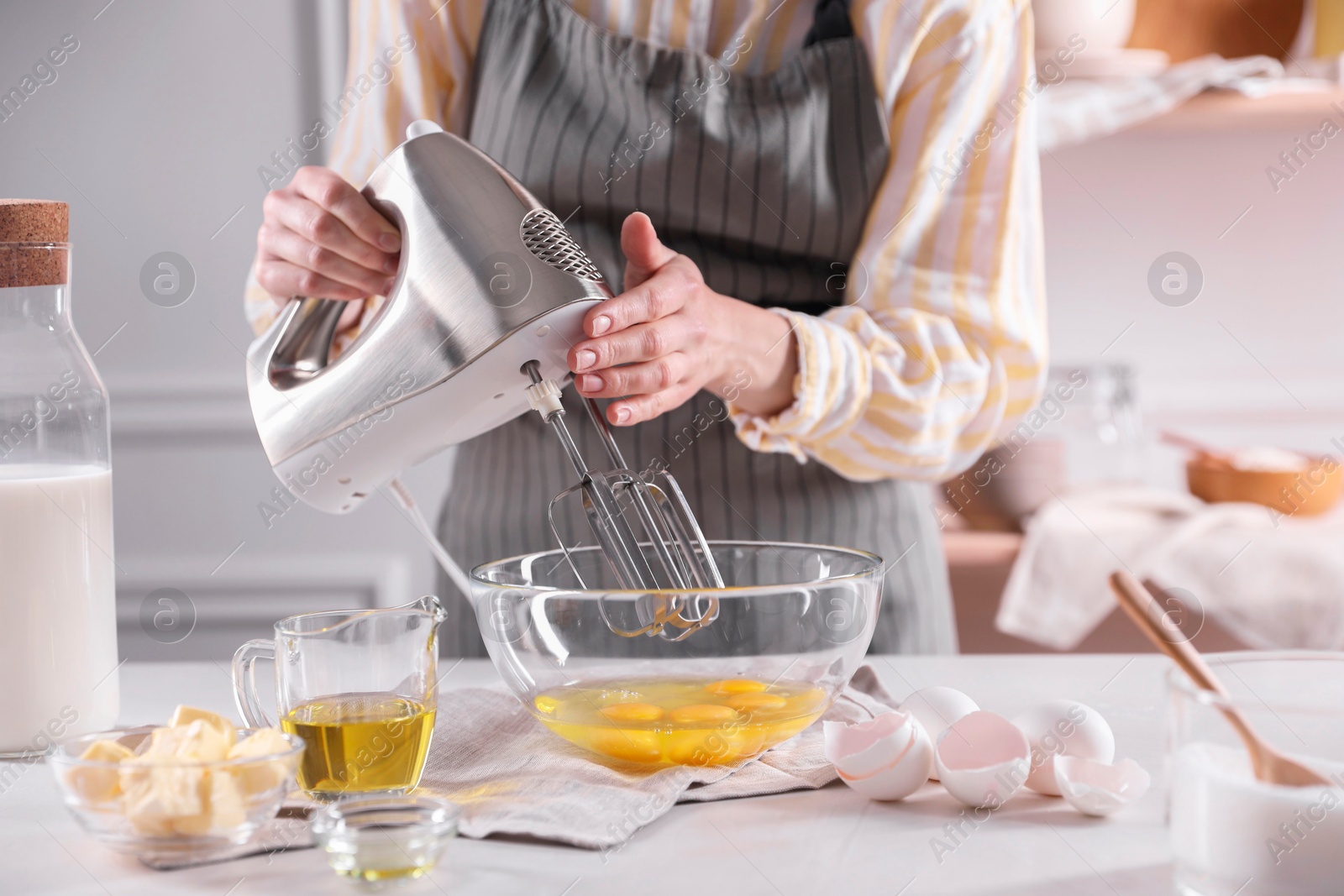 Photo of Woman making dough with mixer in bowl at table, closeup