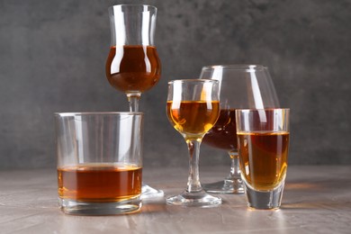 Many different liqueurs in glasses on grey textured table, closeup