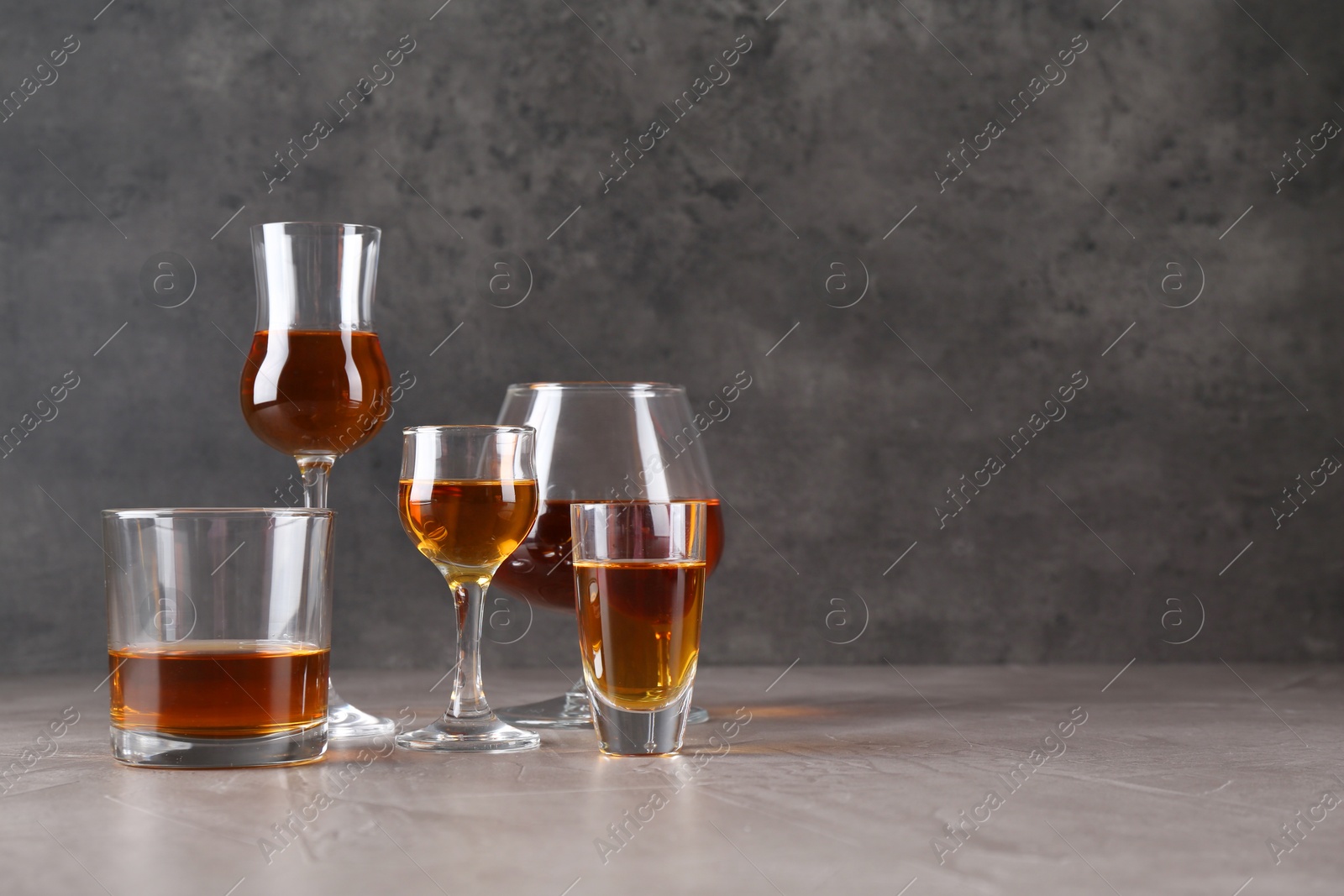 Photo of Many different liqueurs in glasses on grey textured table. Space for text