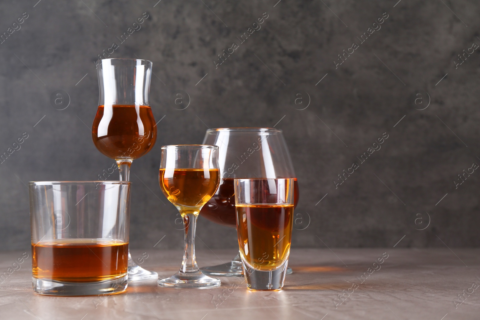 Photo of Many different liqueurs in glasses on grey textured table. Space for text