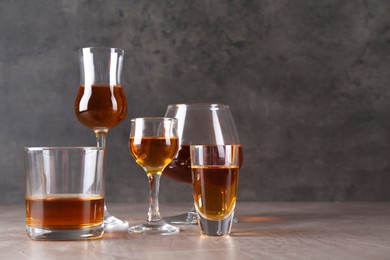 Many different liqueurs in glasses on grey textured table. Space for text