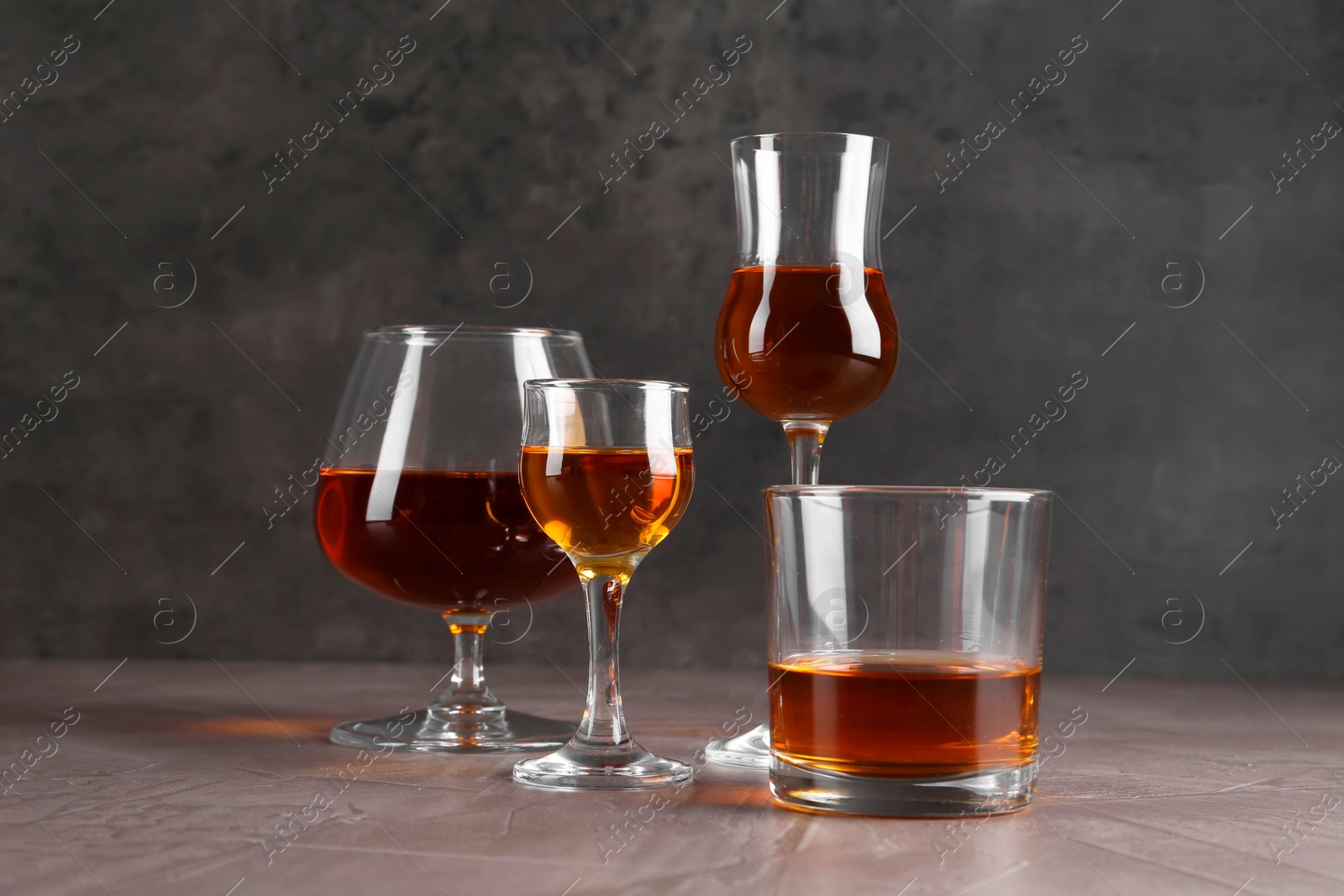 Photo of Many different liqueurs in glasses on grey textured table