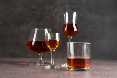 Photo of Many different liqueurs in glasses on grey textured table