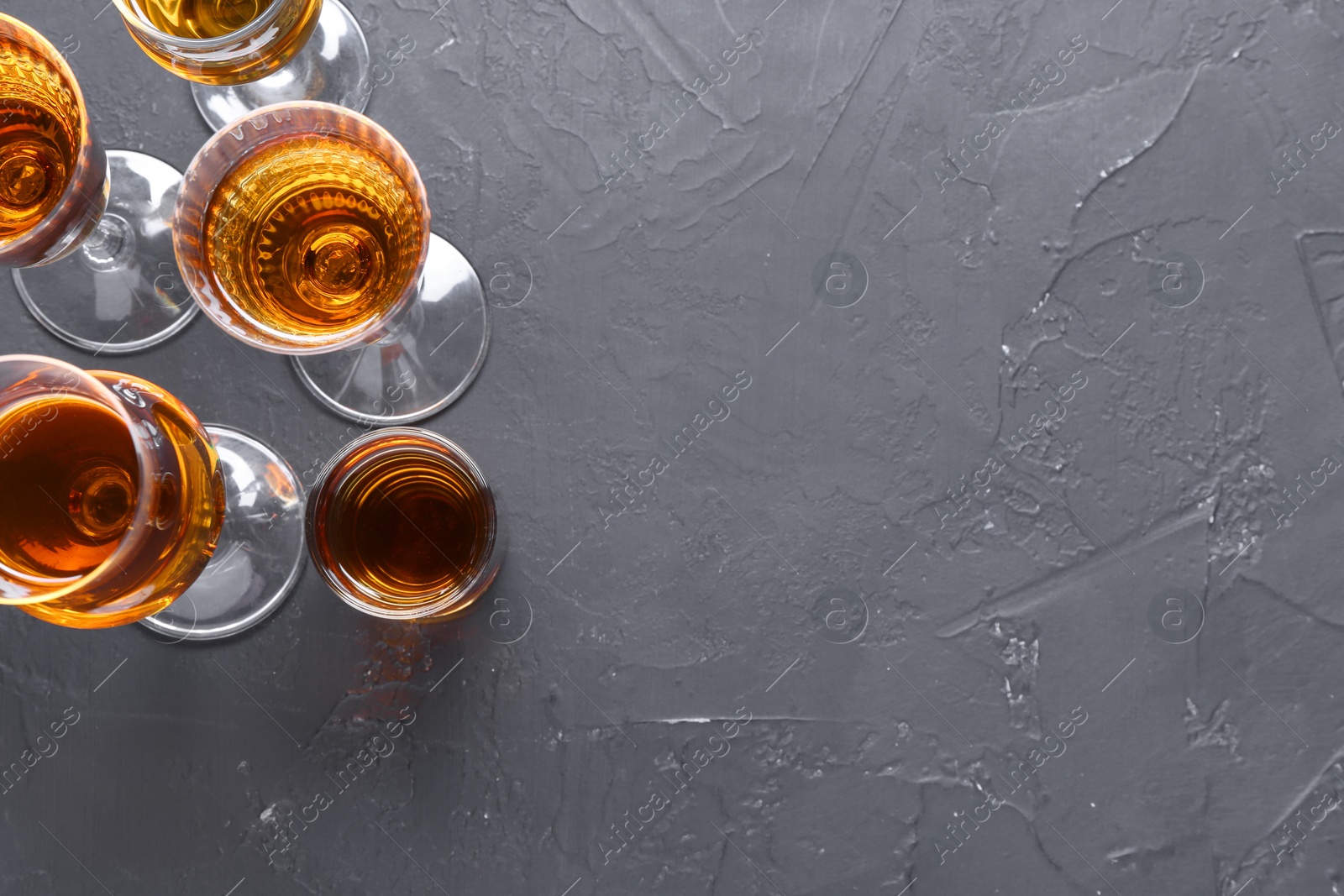 Photo of Many different liqueurs in glasses on dark textured table, flat lay. Space for text