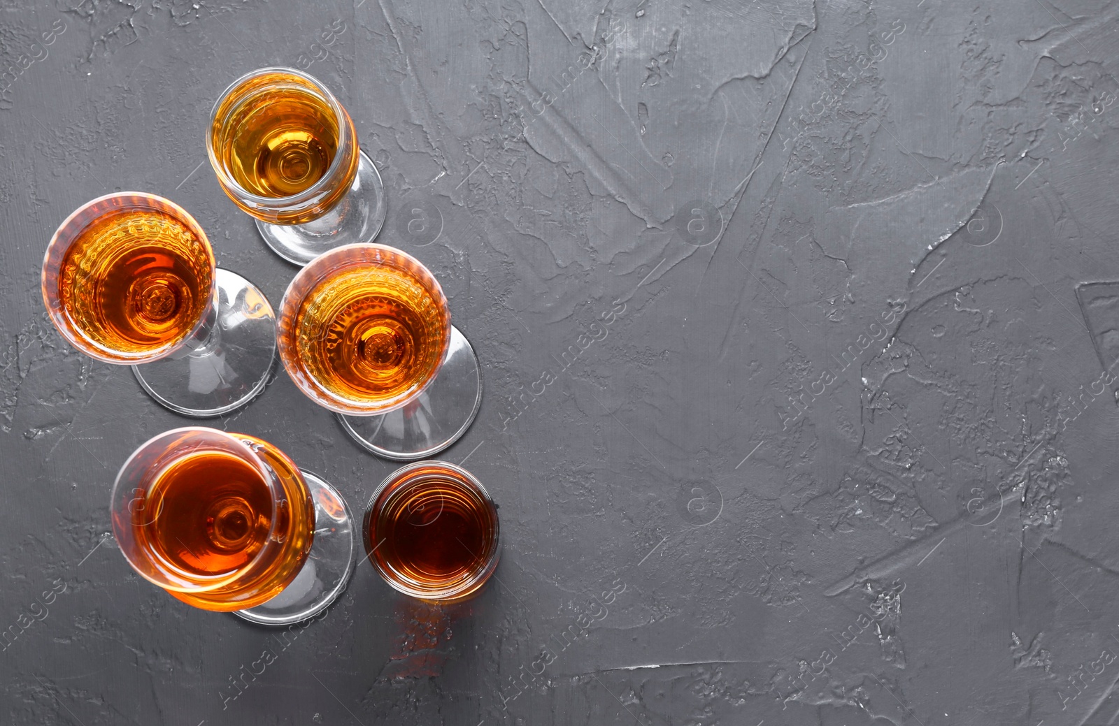 Photo of Many different liqueurs in glasses on dark textured table, flat lay. Space for text