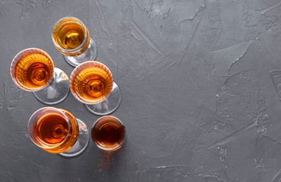 Many different liqueurs in glasses on dark textured table, flat lay. Space for text