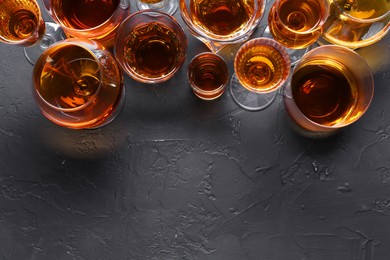 Photo of Many different liqueurs in glasses on dark textured table, flat lay. Space for text