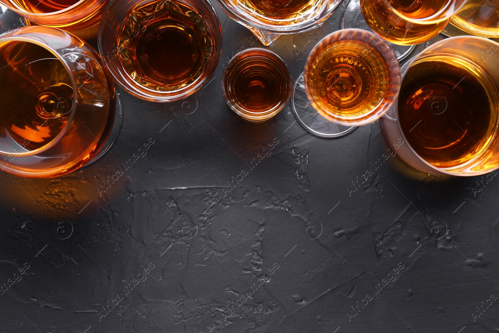 Photo of Many different liqueurs in glasses on dark textured table, flat lay. Space for text