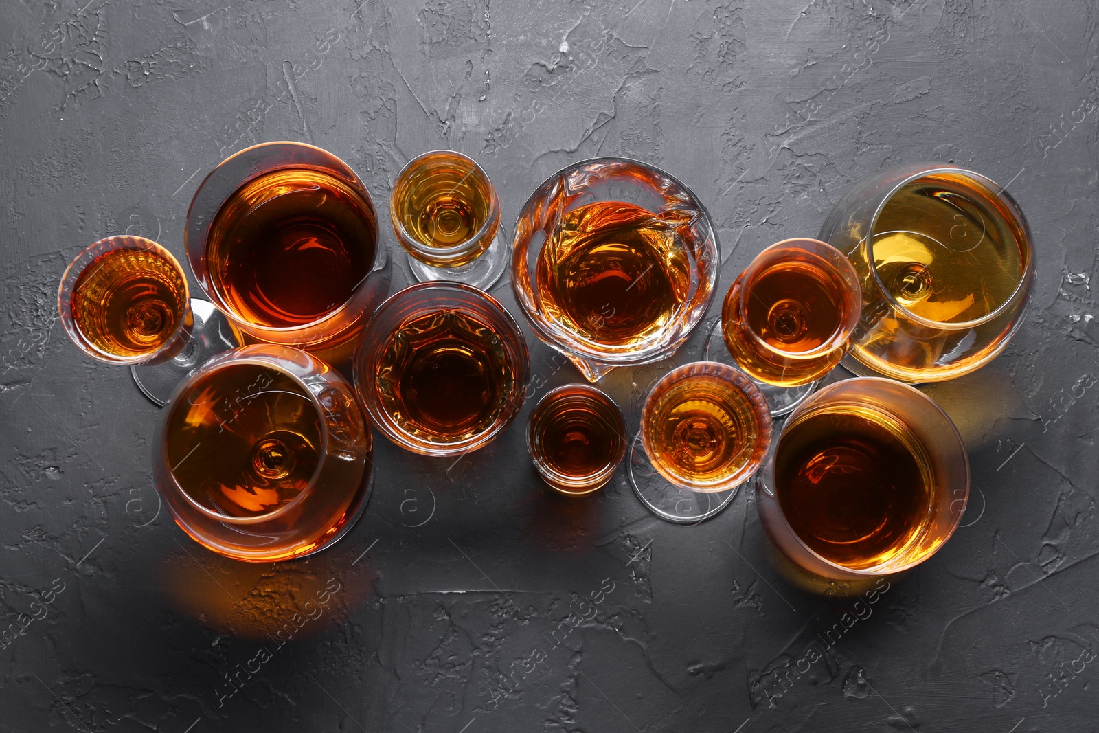 Photo of Many different liqueurs in glasses on dark textured table, flat lay