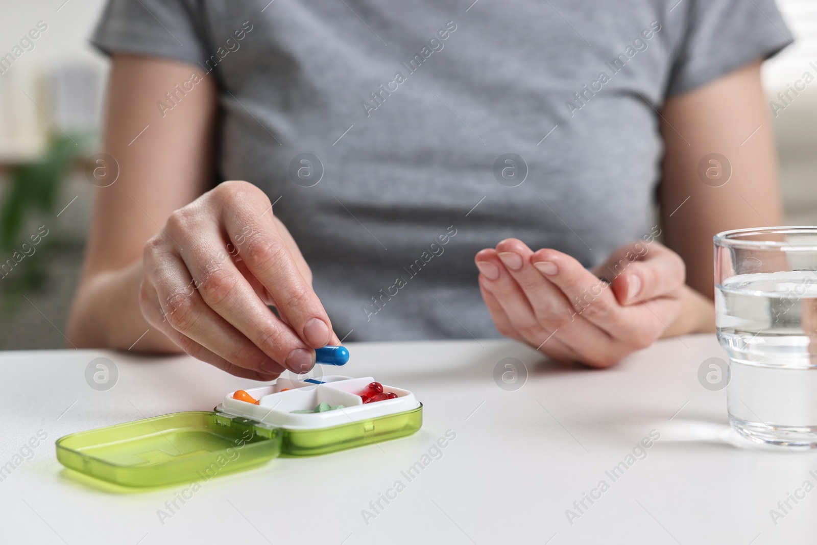 Photo of Woman with pills, organizer and glass of water at white table, closeup