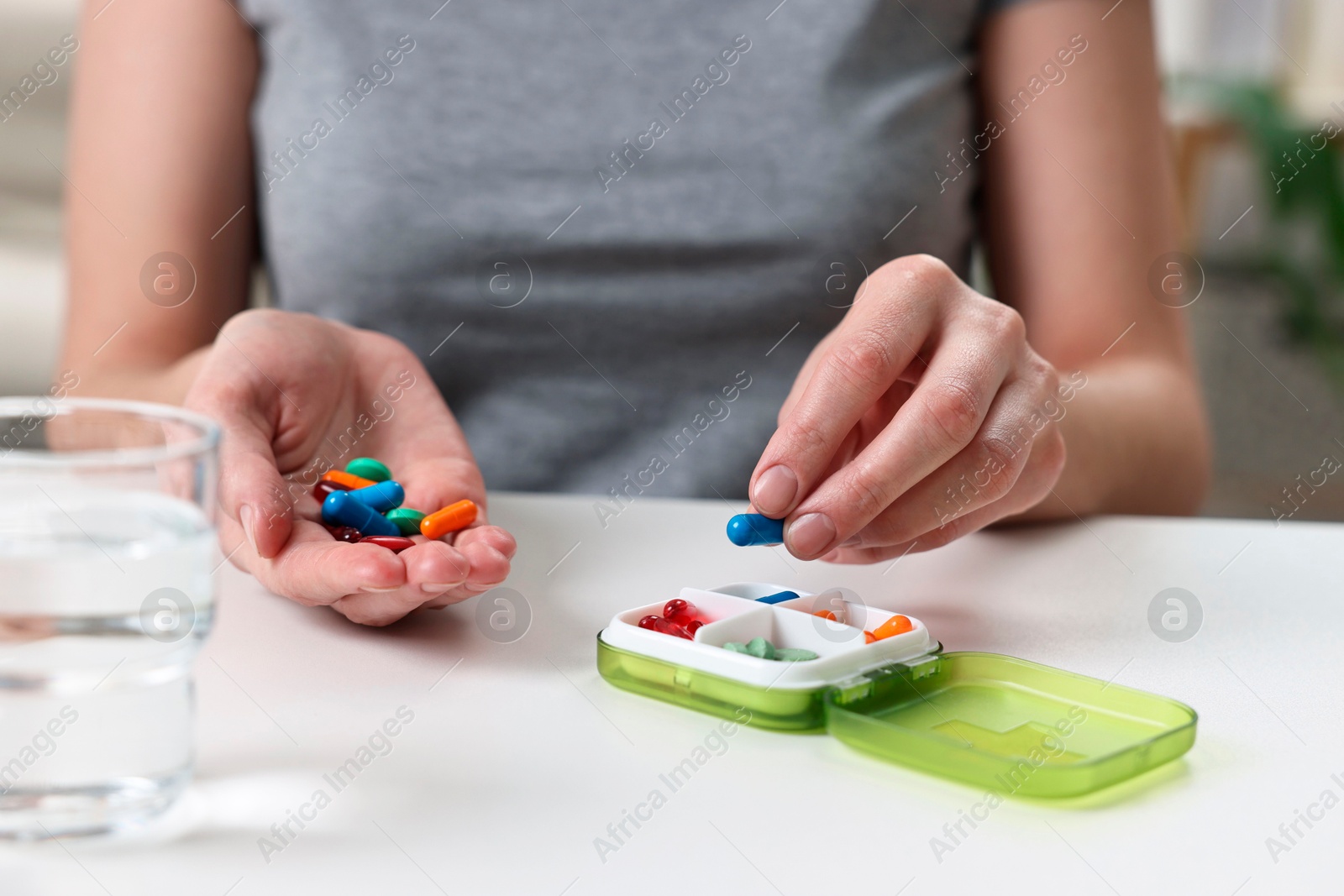 Photo of Woman with pills, organizer and glass of water at white table, closeup