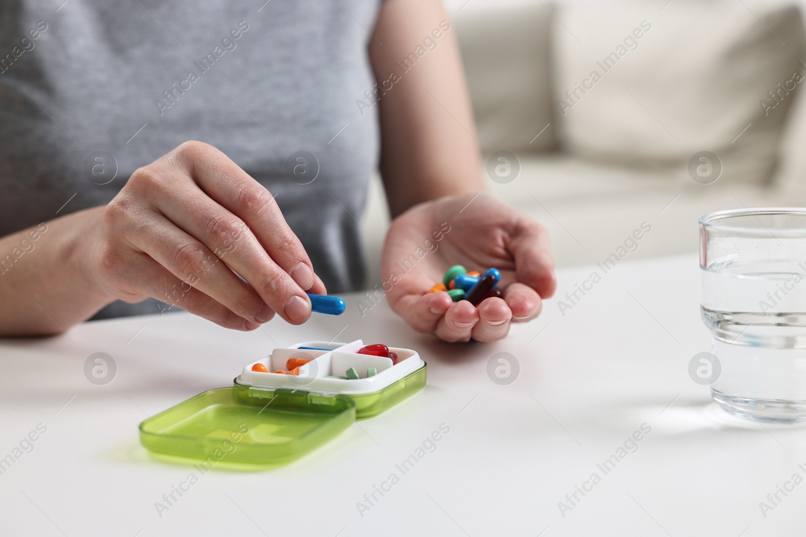 Photo of Woman with pills, organizer and glass of water at white table, closeup