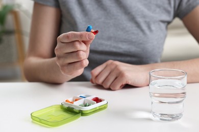 Woman with pills, organizer and glass of water at white table, closeup