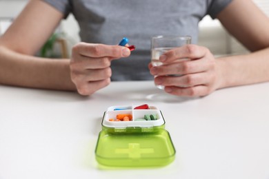 Woman with pills, organizer and glass of water at white table, closeup