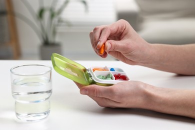 Photo of Woman with pills, organizer and glass of water at white table, closeup