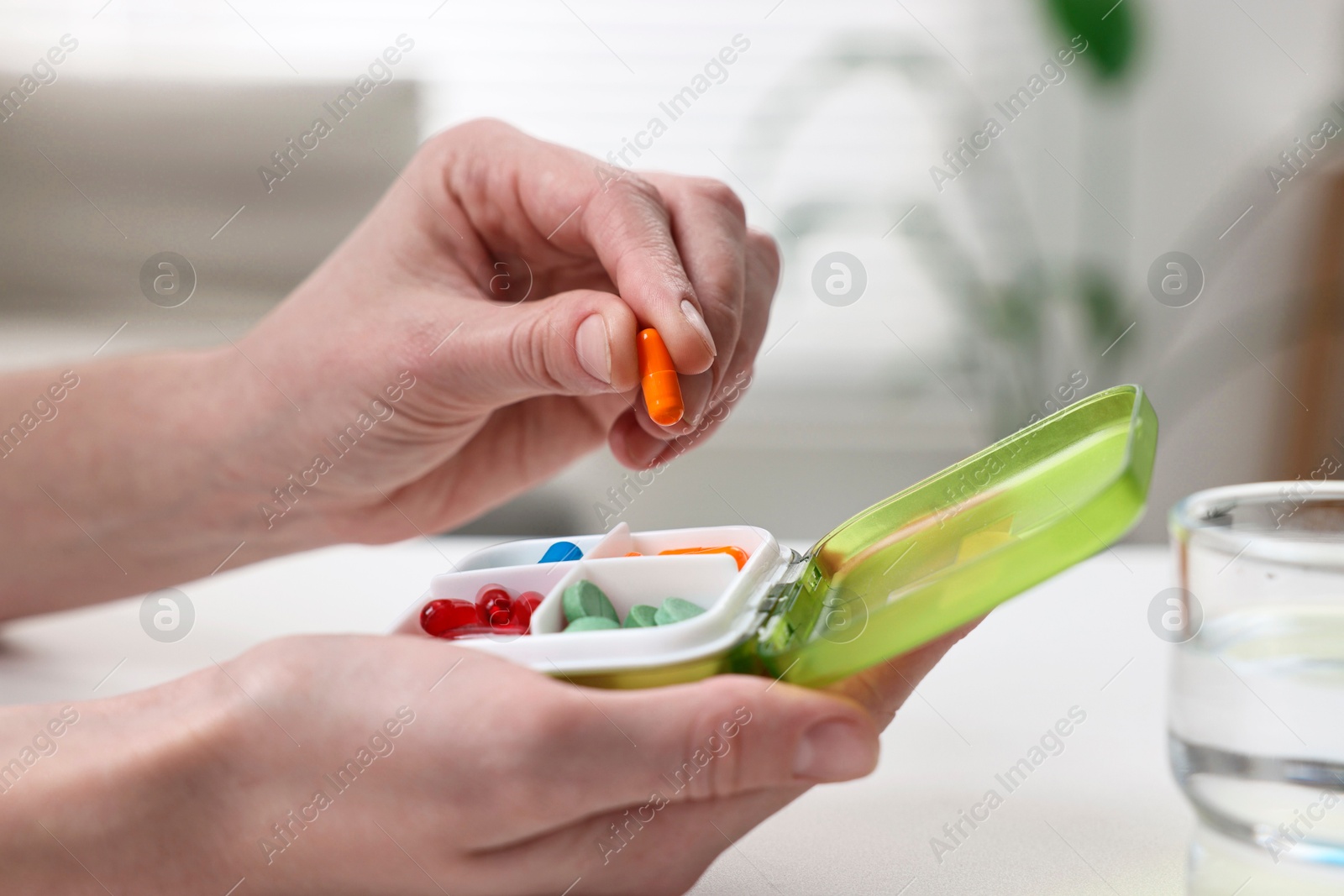 Photo of Woman with pills, organizer and glass of water at white table, closeup