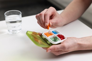 Woman with pills, organizer and glass of water at white table, closeup