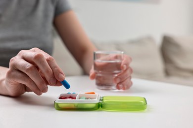 Woman with pills, organizer and glass of water at white table, closeup